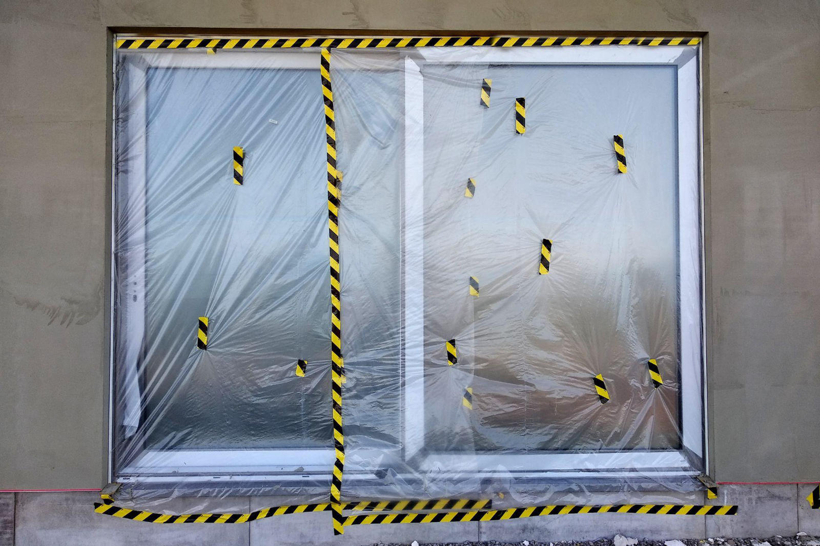 A window in a home under construction sealed with plastic sheeting and caution tape for dust protection.