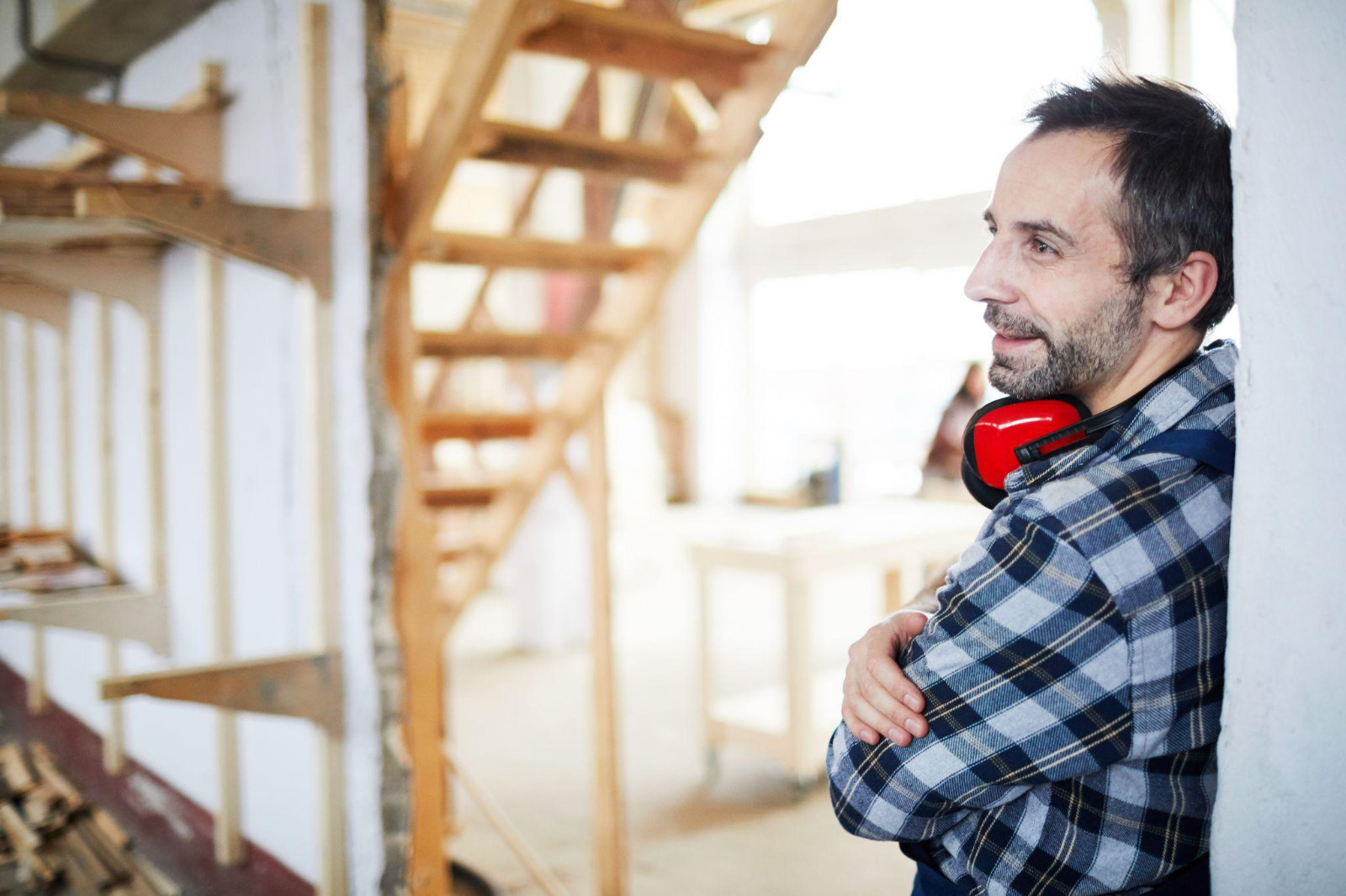 A professional contractor with hearing protection leaning against a wall, thoughtfully considering the project and the homeowner's experience.