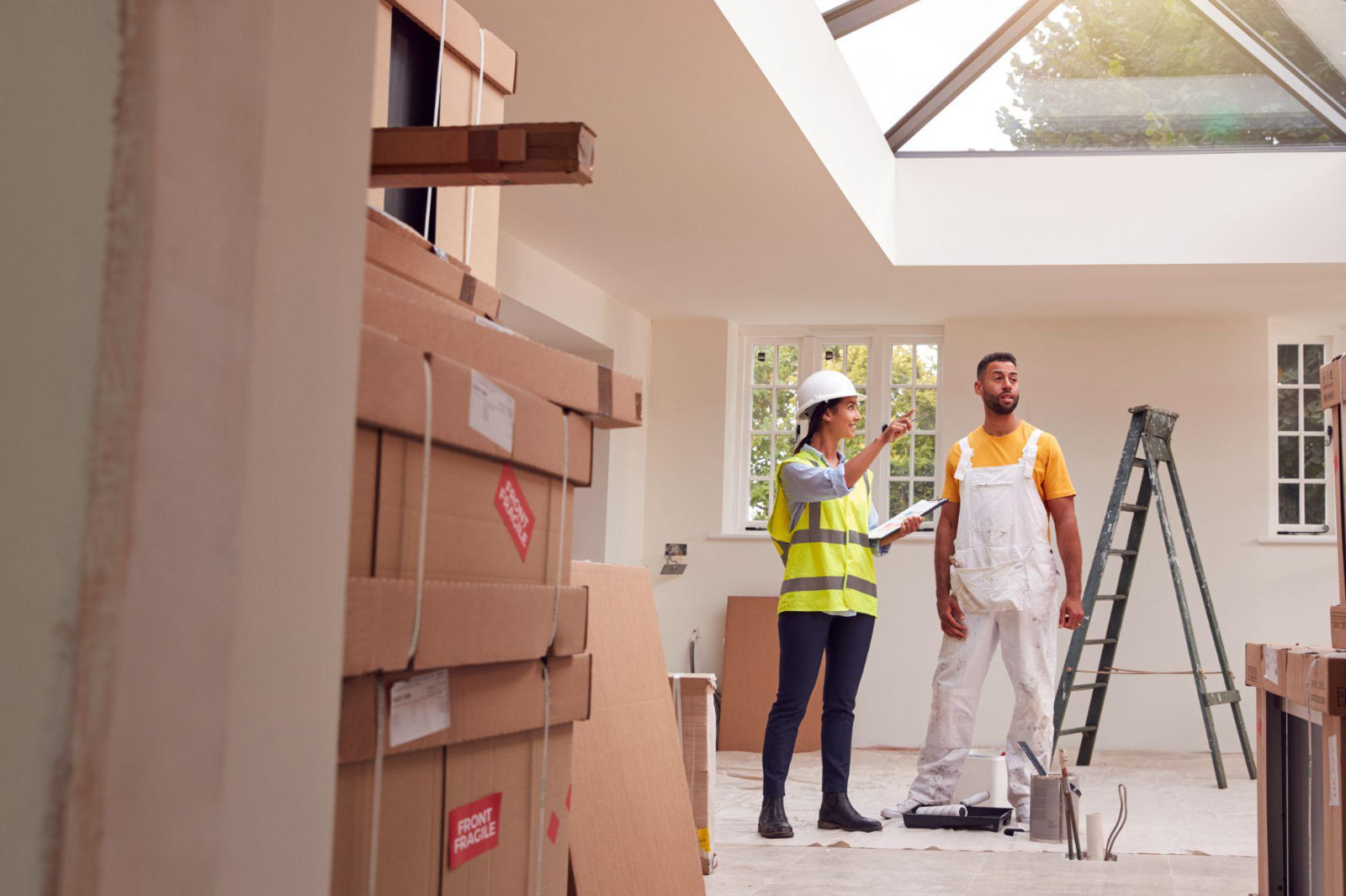 A construction manager and worker discussing renovation plans amidst stacks of cardboard boxes in a home under construction.