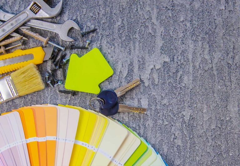 Tools, paint swatches, and keys on a table representing home renovation planning.