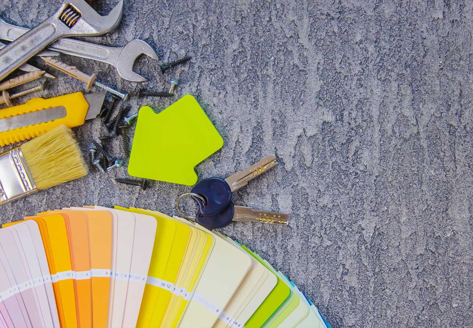 Tools, paint swatches, and keys on a table representing home renovation planning.
