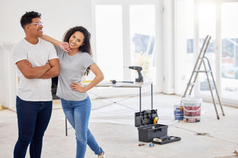 A smiling couple standing in an empty home undergoing renovation, representing a positive and managed remodeling experience.