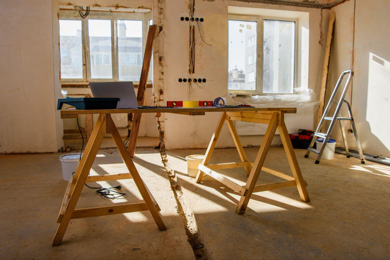 A temporary workspace with a laptop on sawhorses inside a home undergoing renovation.