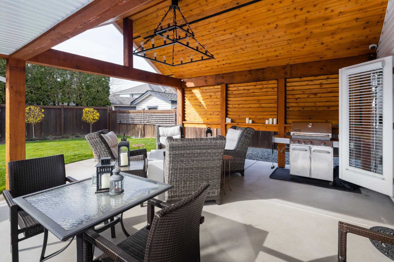 A luxury covered outdoor living space and patio lounge with a wood-paneled ceiling and built-in barbecue area, completed during a custom home building process in BC.