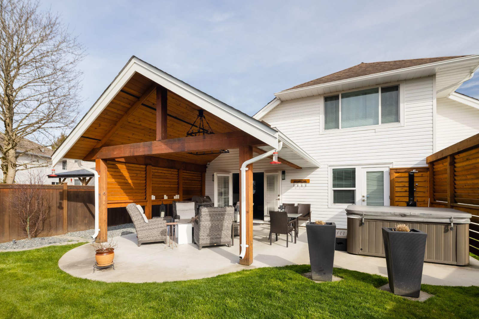 The backyard exterior view of a high-end home renovation featuring a large timber-framed covered patio and hot tub setup, demonstrating the work of a professional builder.