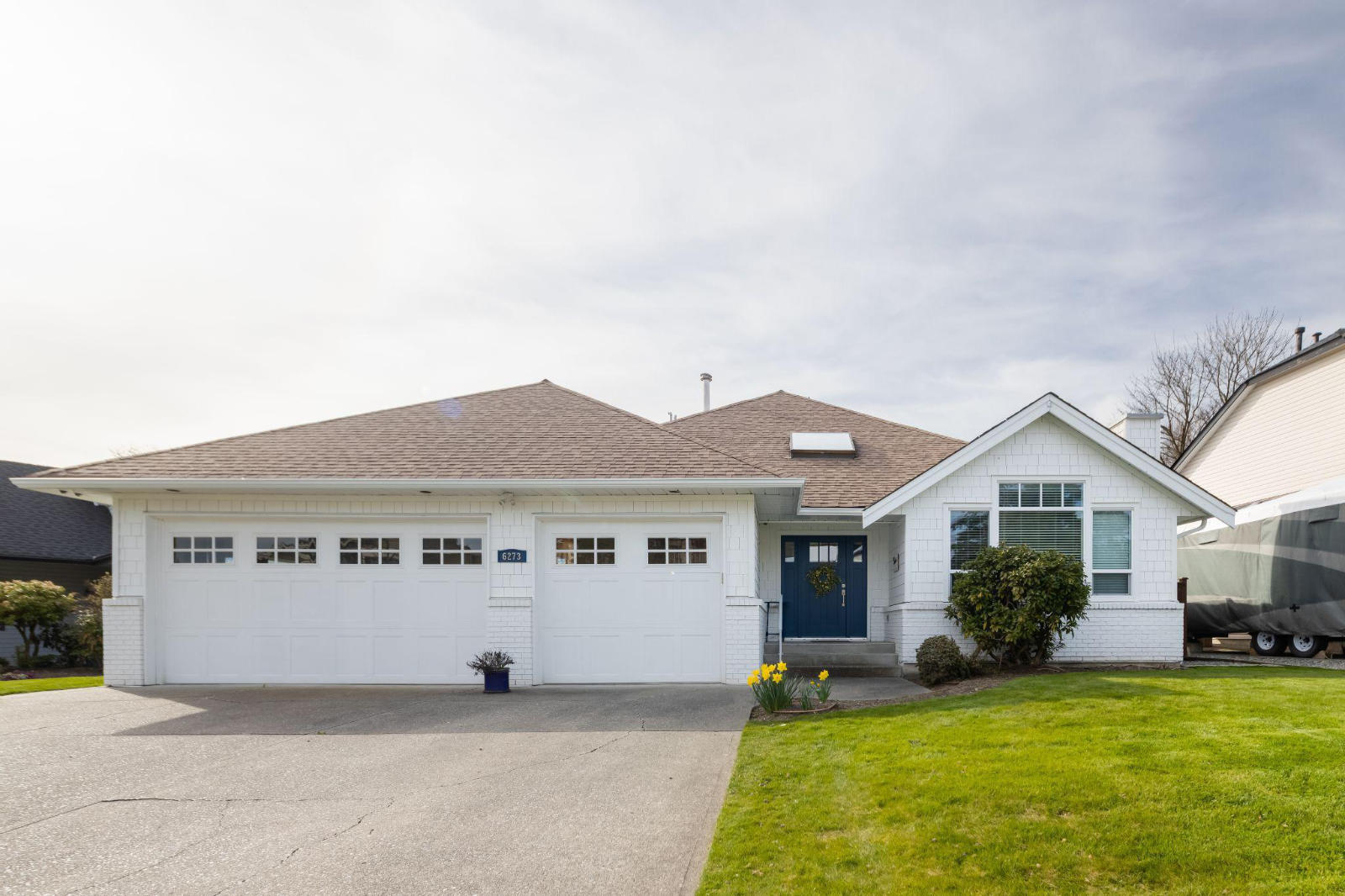 homes-to-havens-custom-home-renovation-bc Exterior view of a beautifully renovated white modern craftsman style home with a blue front door and a three-car garage in British Columbia.