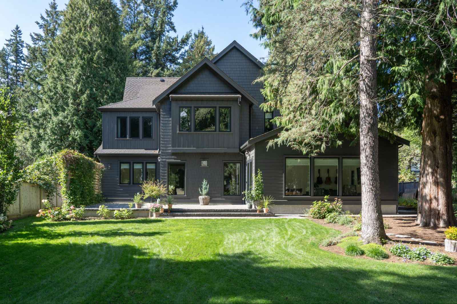 luxury-custom-home-exterior-surrey Exterior view of a modern, dark gray luxury custom home with a manicured green lawn and mature trees in Surrey.