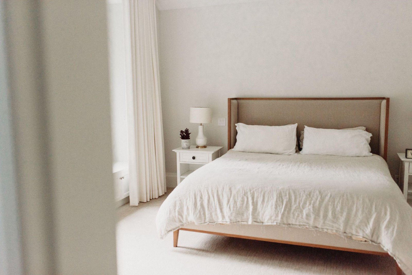 Minimalist luxury bedroom with bright white linens, neutral tones, and elegant drapery in a custom home.