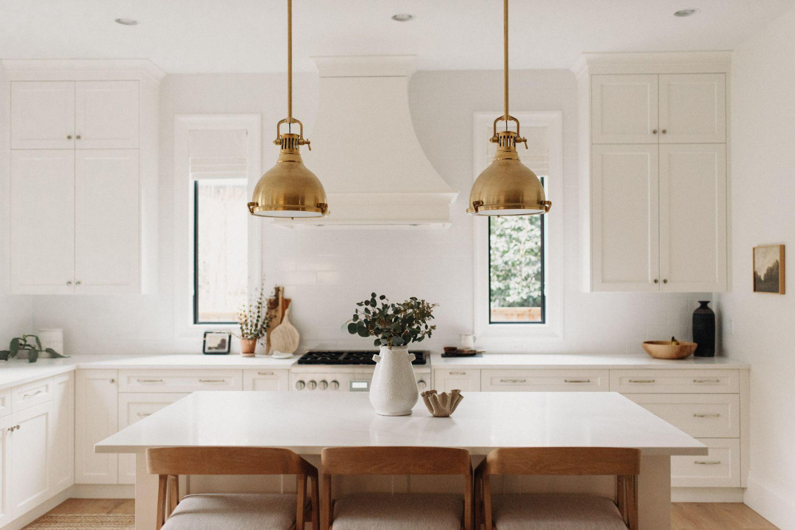 Clean, symmetrical luxury white kitchen featuring high-end cabinetry, a central island, and striking gold pendant lights.