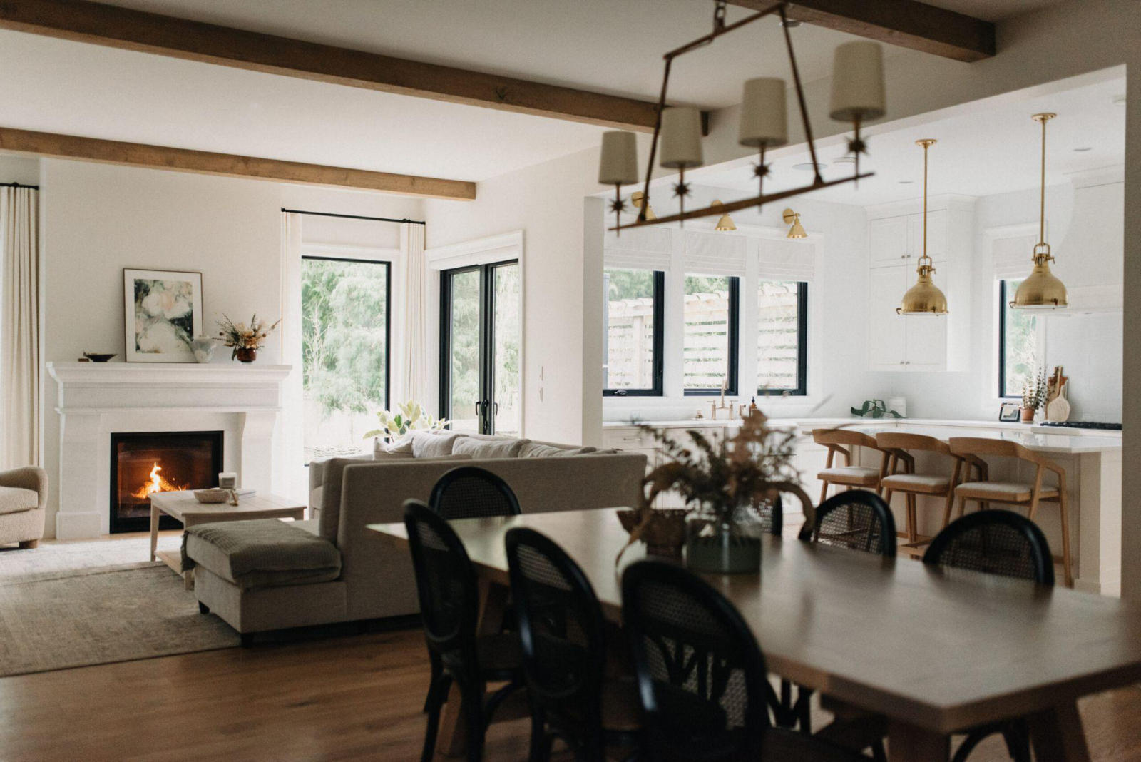 Bright, open-concept luxury home interior featuring a living room with a fireplace, a dining area, and a white kitchen.