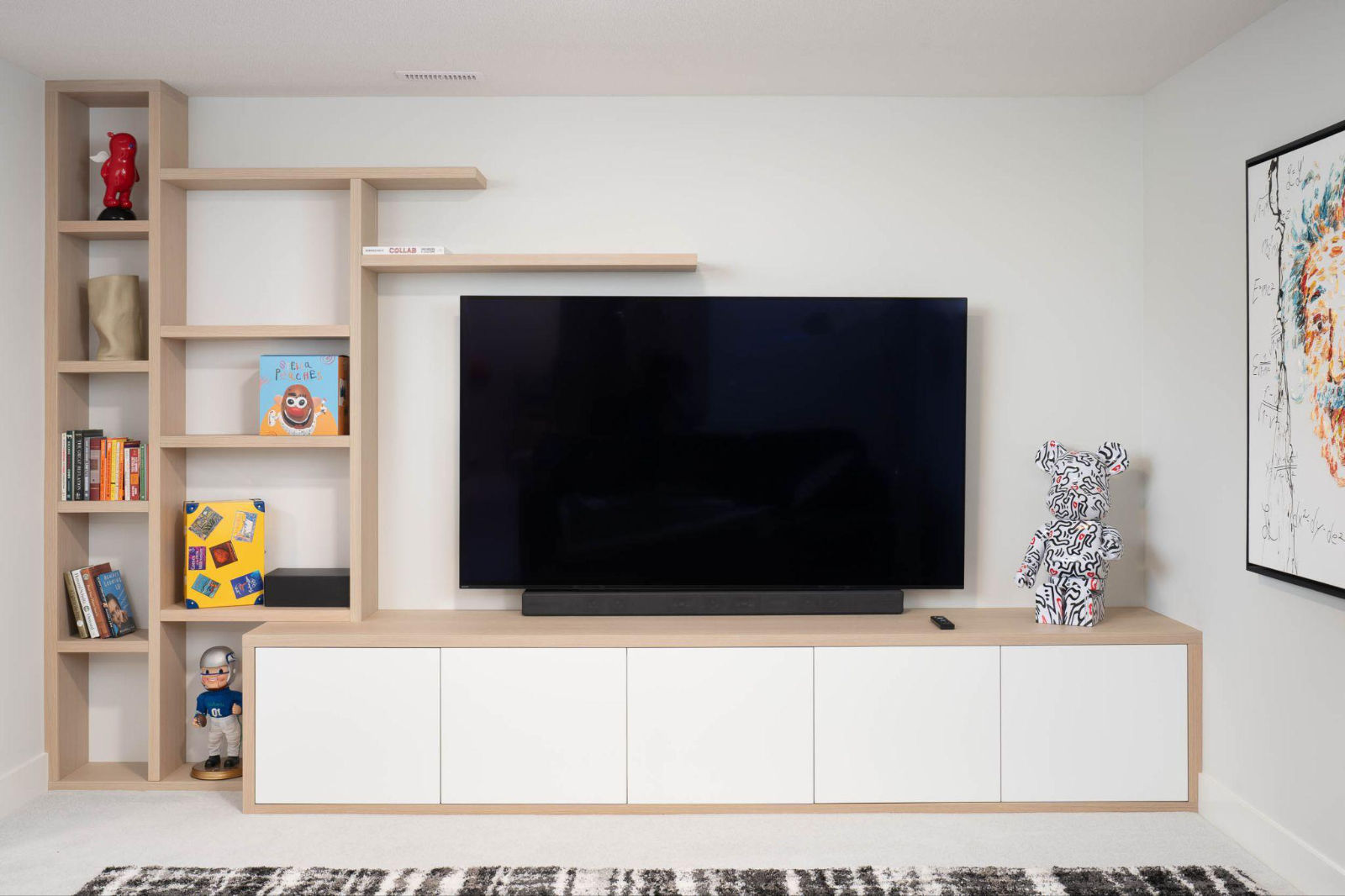 Custom light wood floating shelves and built-in white media console unit with a large television in a renovated living area.