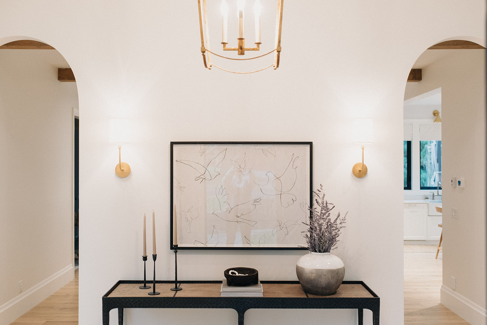 Elegant home foyer with double arched doorways, subtle sconce lighting, and a console table styled with minimalism and art.