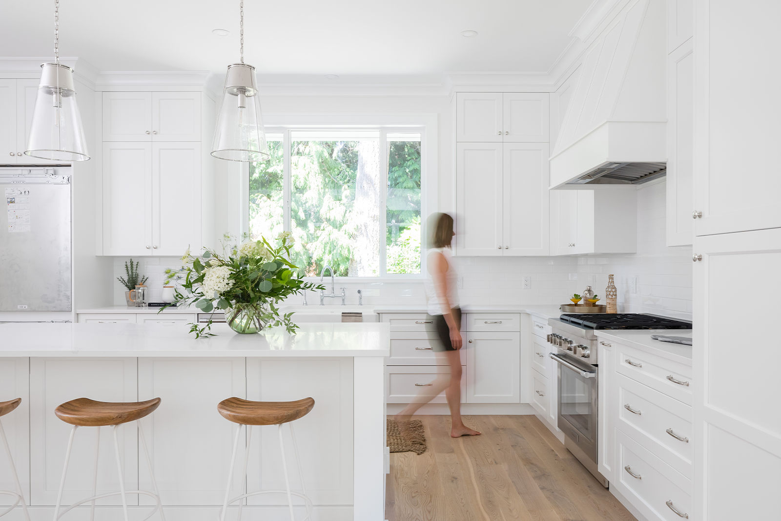 Bright white kitchen with clear walking paths, showing natural movement between the island seating, sink, and gas range.