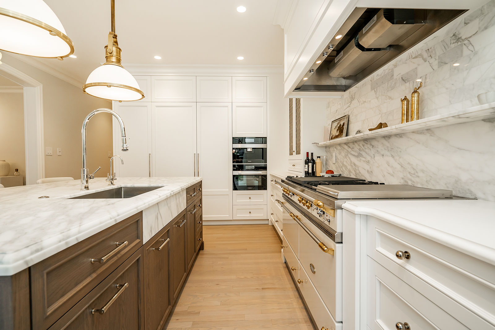 Custom luxury kitchen island featuring rich wood cabinets, a marble farm sink, brass hardware, and a high-end gas range.