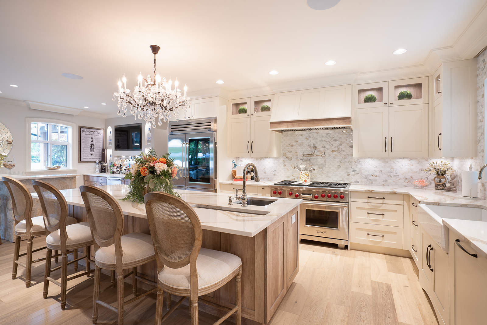 Elegant luxury kitchen renovation featuring a wooden island with plush stool seating, crystal chandelier, stainless steel appliances, and custom cabinetry.